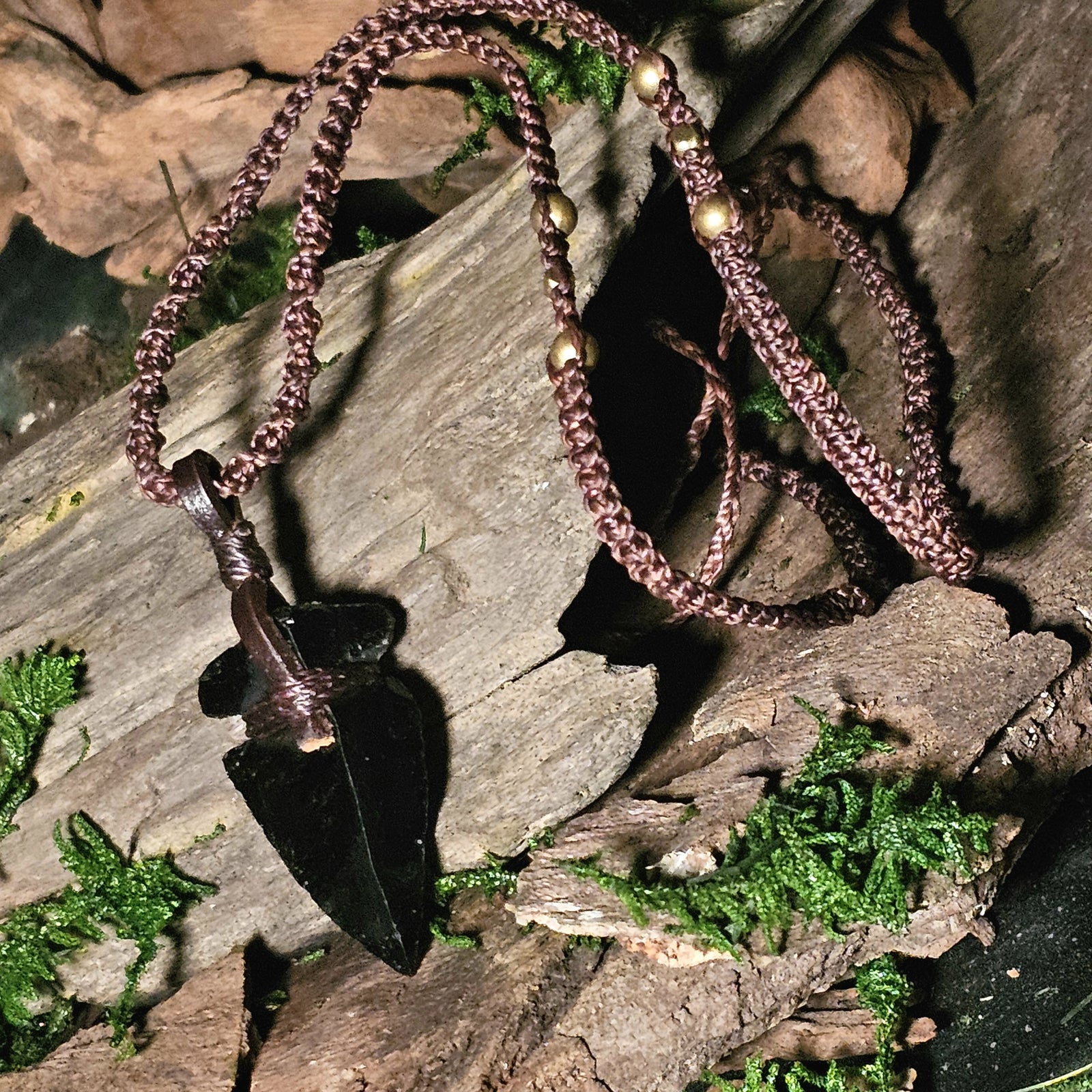 Black obsidian arrowhead pendant on rustic bark background