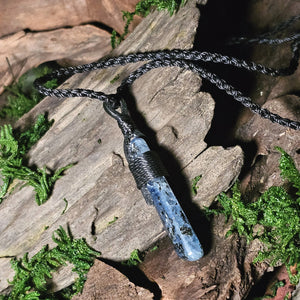 Blue kyanite pendant positioned on cracked wood and lichen