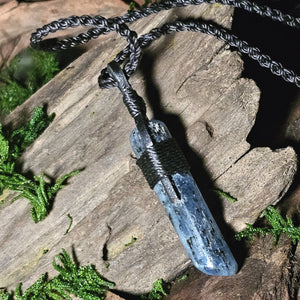 Close-up of polished kyanite pendant on black cord over bark