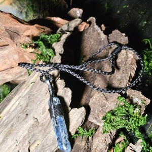 Long kyanite pendant wrapped in waxed thread, placed on driftwood