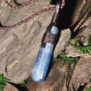 Artisan kyanite crystal pendant on braided brown cord over driftwood