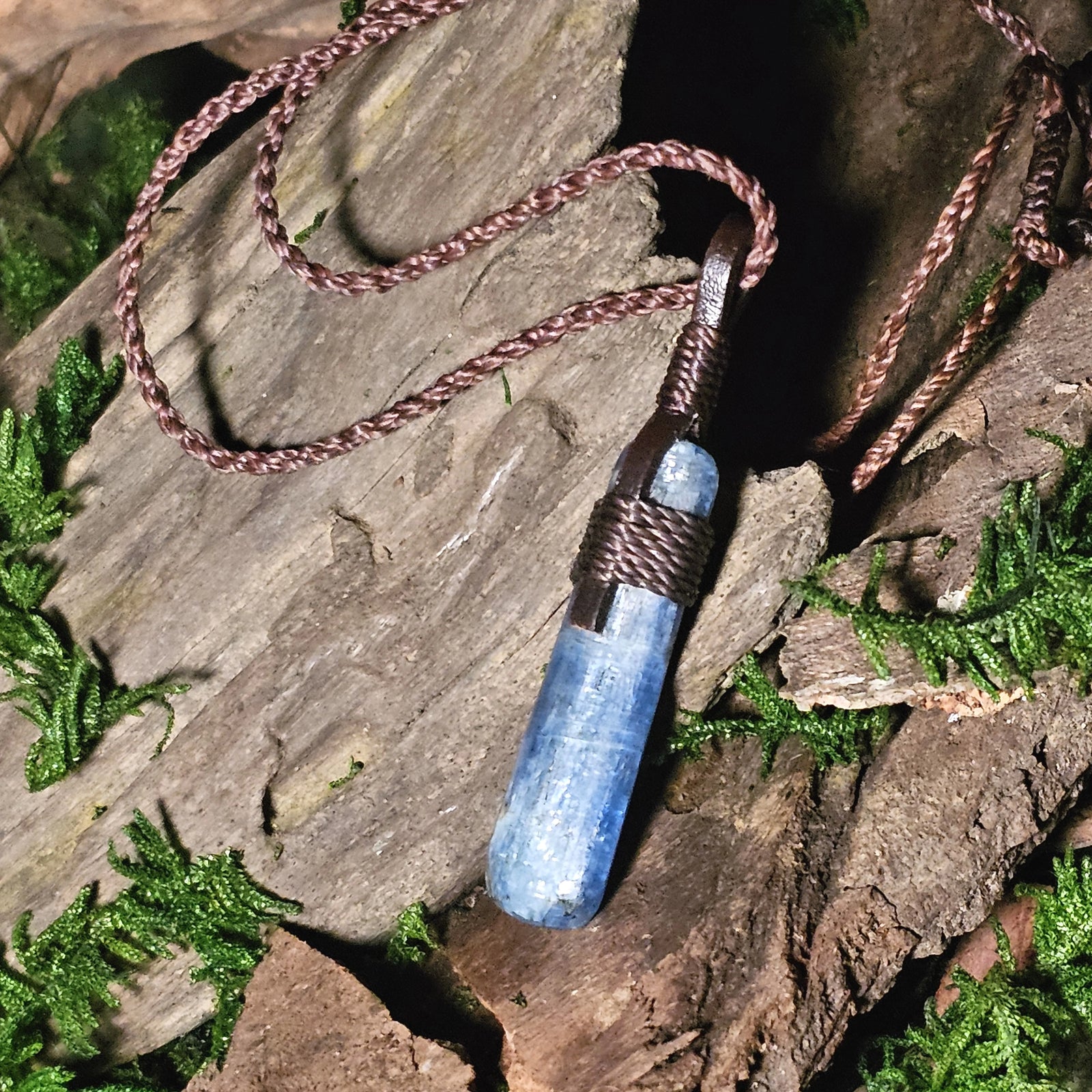 Blue kyanite pendant wrapped in brown cord, resting on rustic wood