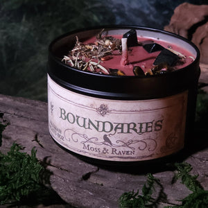 Candle labeled 'Boundaries' by Moss & Raven on a wooden surface with greenery.