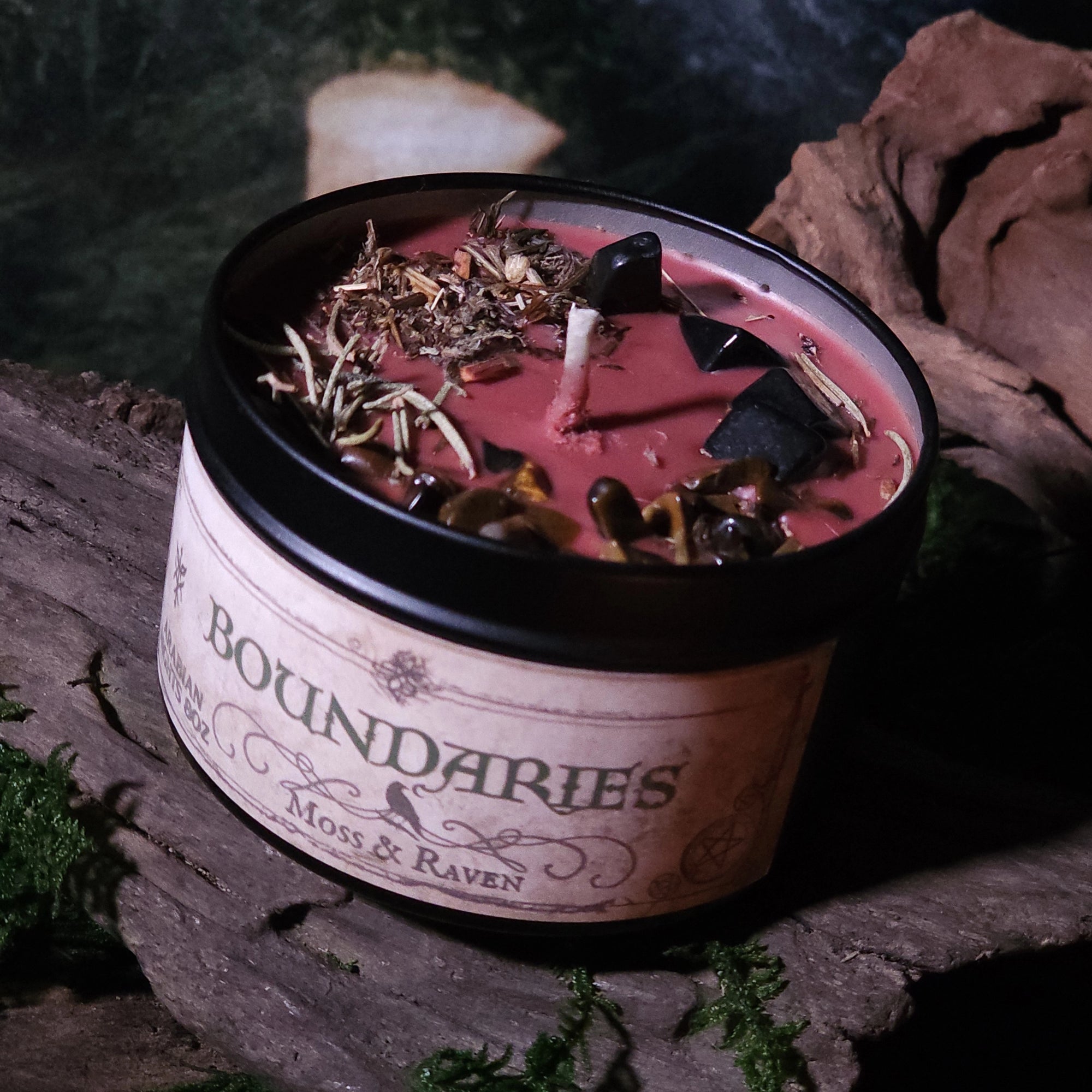 Candle in a container labeled 'Boundaries' with natural elements on top, placed on a stone surface.