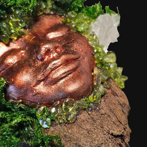 Close-up of copper-bronze Forest Guardian face framed by moss and crystals — symbol of natural growth and steady renewal.