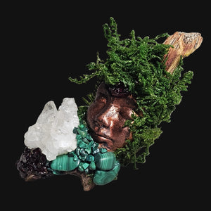 Forest Guardian statue resting on driftwood, adorned with deep green moss, Malachite, Garnet, and Clear Quartz — handcrafted by Moss & Raven.