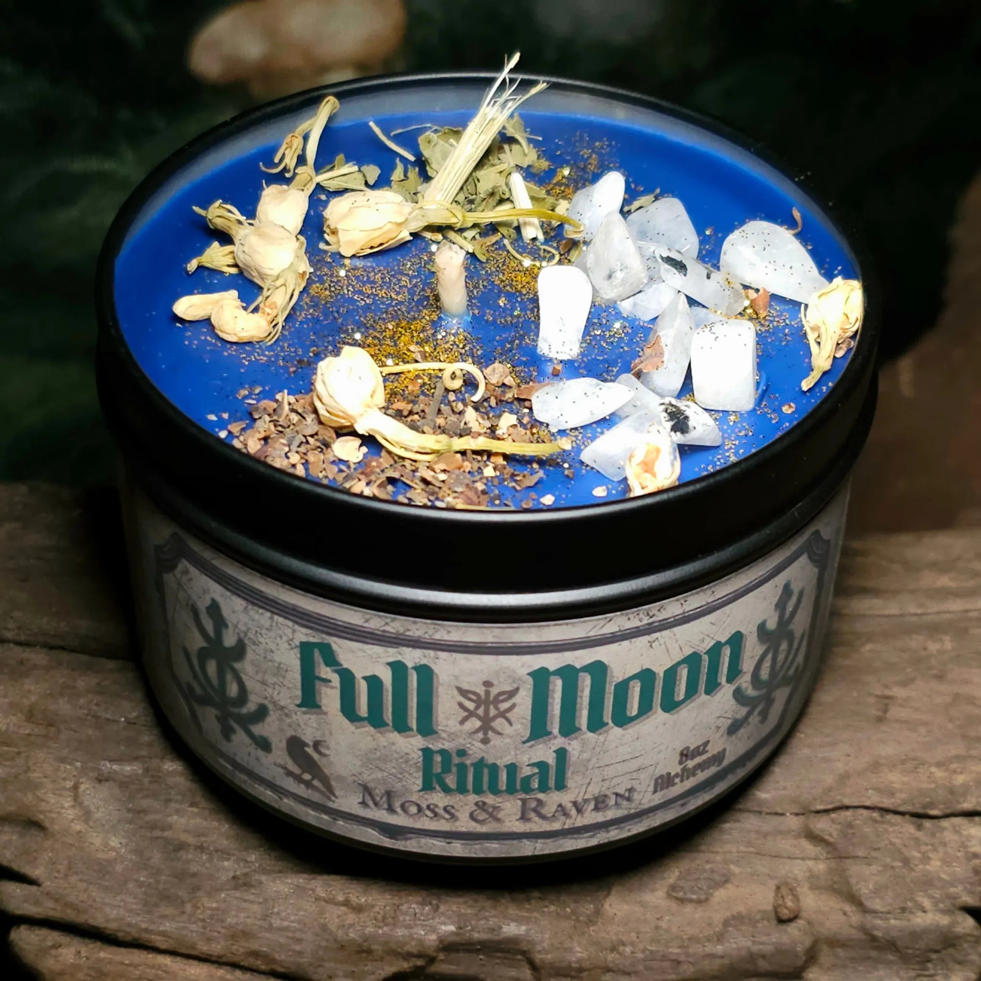 Full Moon Ritual Candle by Moss & Raven – blue wax candle in black tin, dressed with moonstone chips, jasmine flowers, bladderwrack, and passionflower