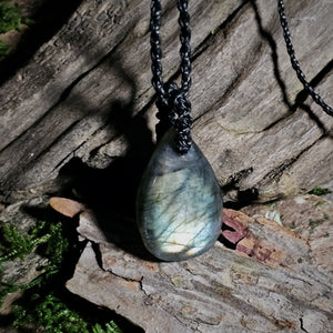 Teardrop-shaped labradorite pendant on a against a driftwood surface with natural light