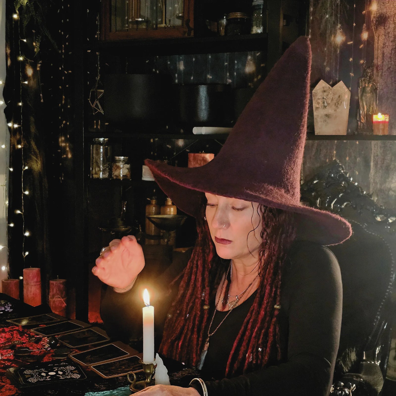 Ness from Moss & Raven holding space for a candlelit mediumship reading, seated in a dark ritual room with spirit tools and crystals.