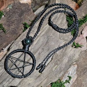 Handwoven black pentacle talisman necklace with moss agate bead resting on natural wood