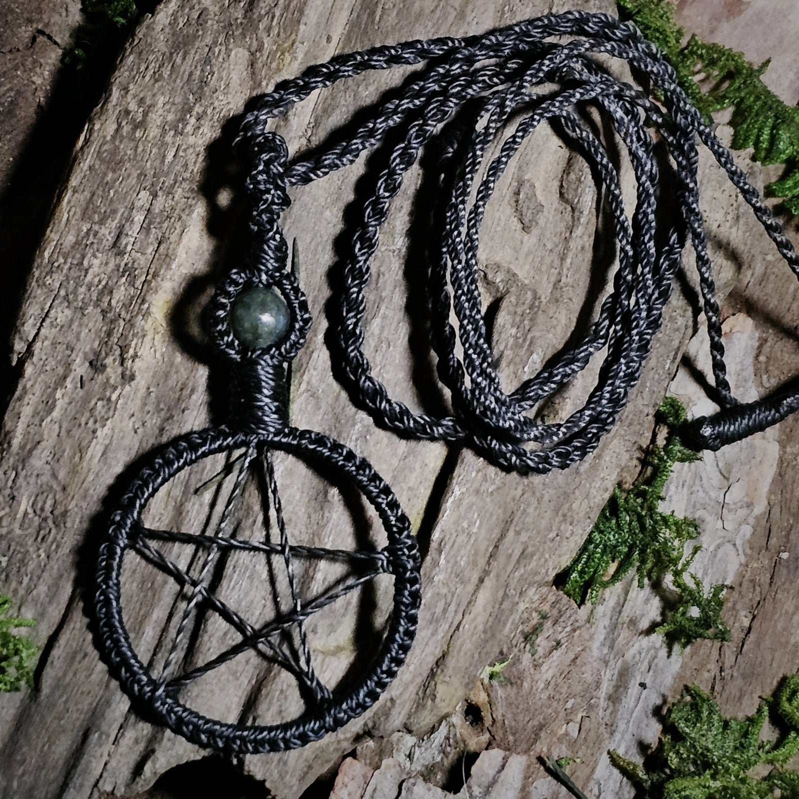 Black pentacle talisman necklace with moss agate bead resting on natural bark
