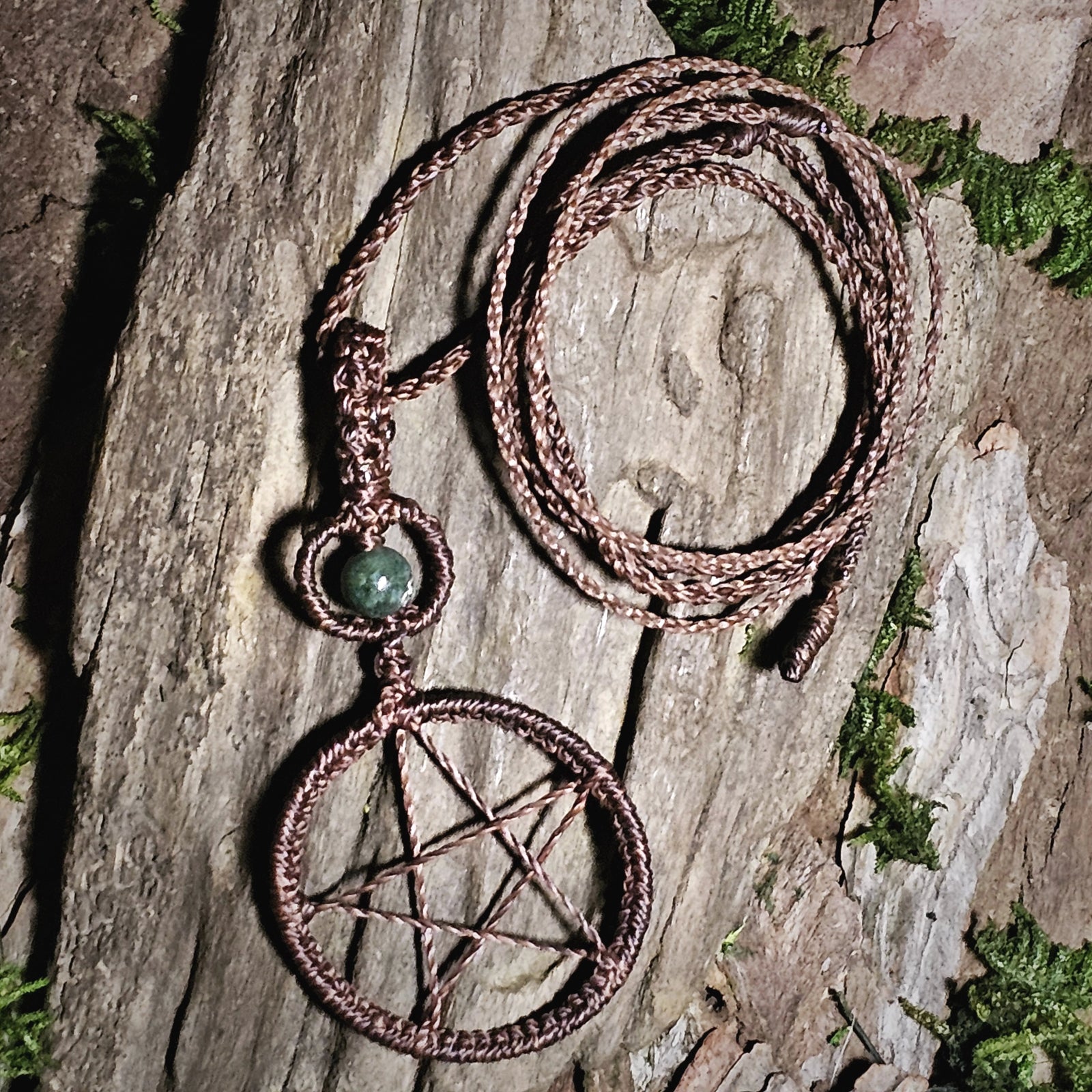 Brown pentacle talisman necklace with moss agate bead resting on natural wood