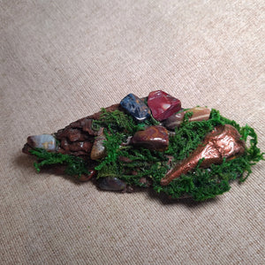 Driftwood altar with moss, red jasper, mookaite, and pietersite crystals beside a sculpted copper raven – The Raven’s Nook by Moss & Raven.