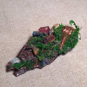 Close-up of copper raven among green moss and polished grounding stones on aged wood.