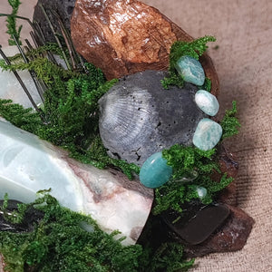 Close-up of pale Amazonite point surrounded by dark grounding stones and green moss.