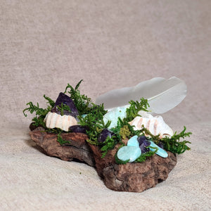 Natural driftwood base adorned with ocean shells, crystals, and a white feather for calm and clarity.
