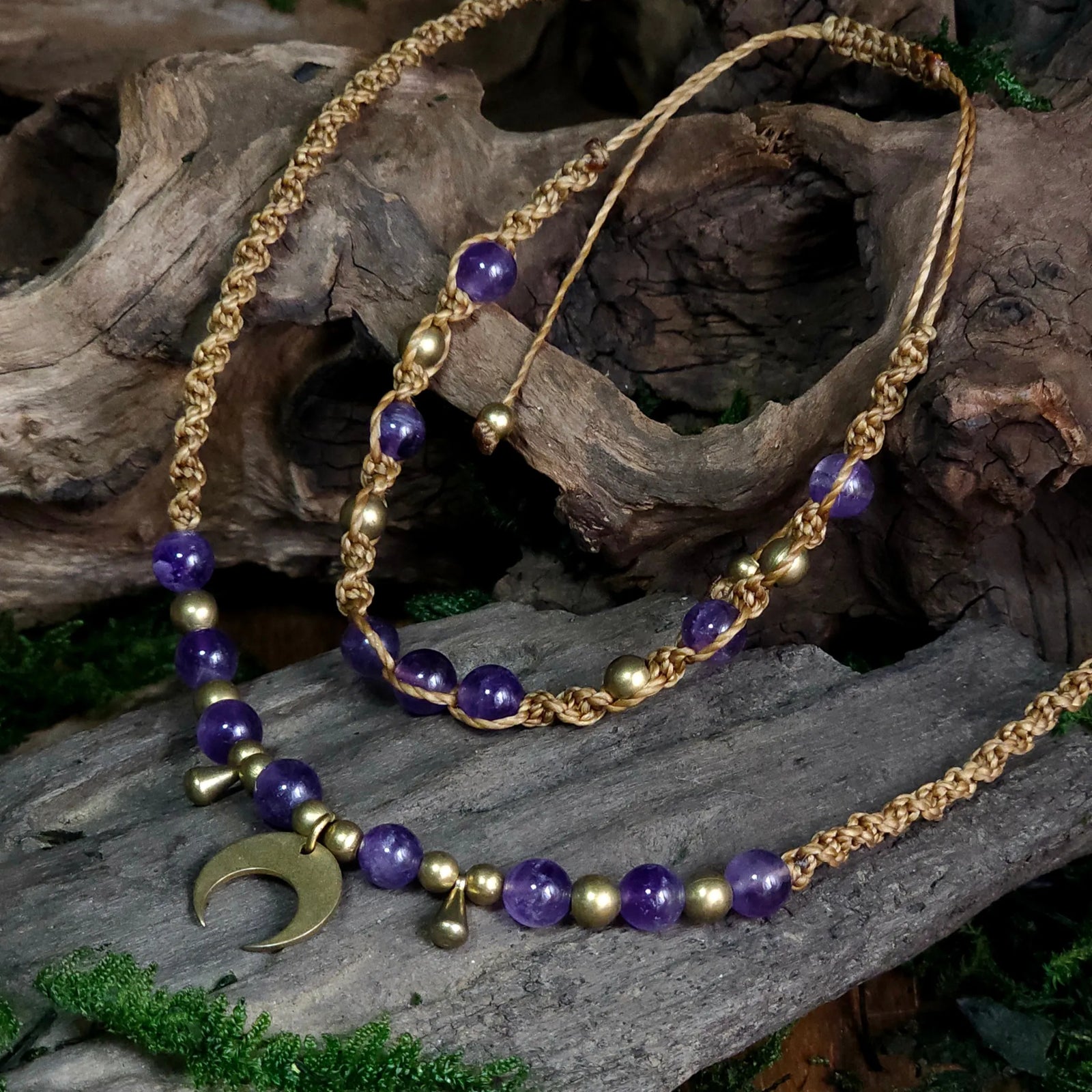 Handwoven golden cord necklace and bracelet set featuring amethyst beads, brass accents, and a brass crescent moon pendant, displayed on driftwood with moss.