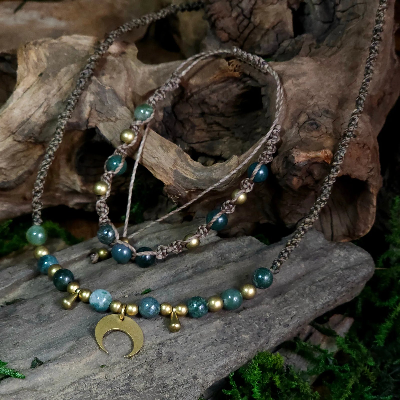 Earth-toned necklace and bracelet set with moss agate beads, hand-braided cord, brass accents, and a brass crescent moon pendant, styled on driftwood with moss.