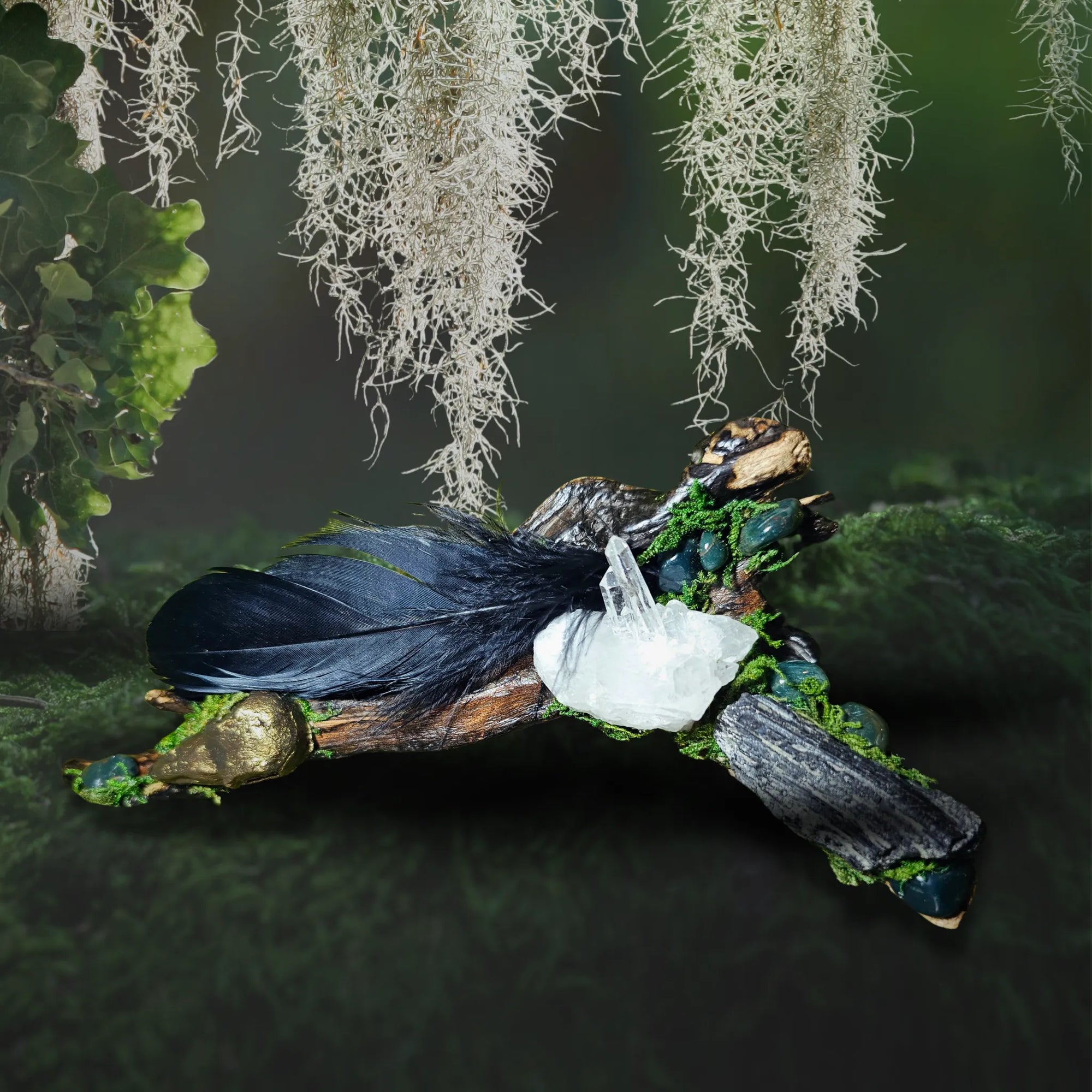Raven’s Mark crystal forest by Moss & Raven shown on moss background. Includes gold raven head, Black Tourmaline, Bloodstone, feather, and moss-covered driftwood.