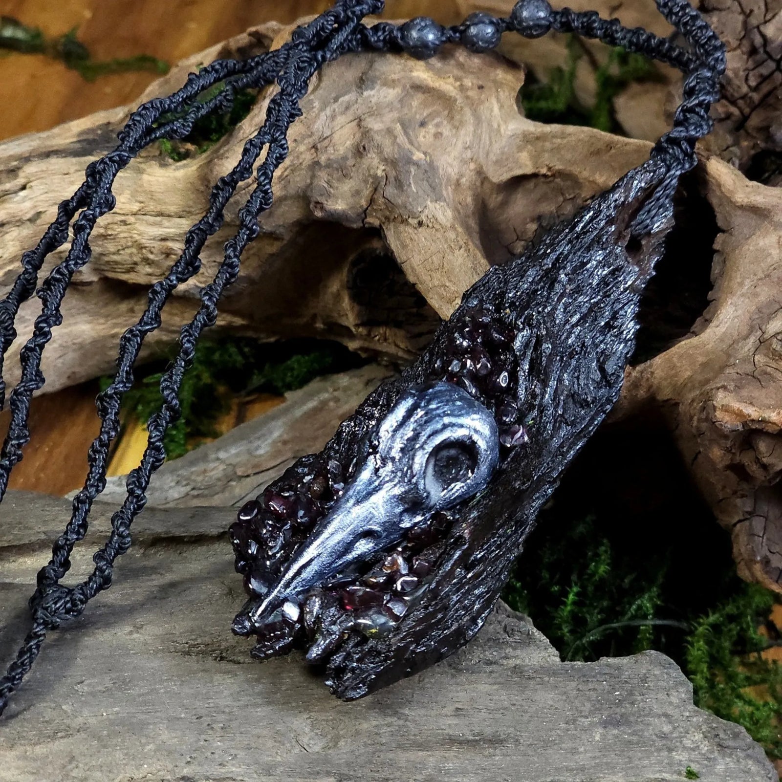 Angled view of Warrior’s Heart Talisman resting on driftwood, showcasing the garnet detail and natural texture.

