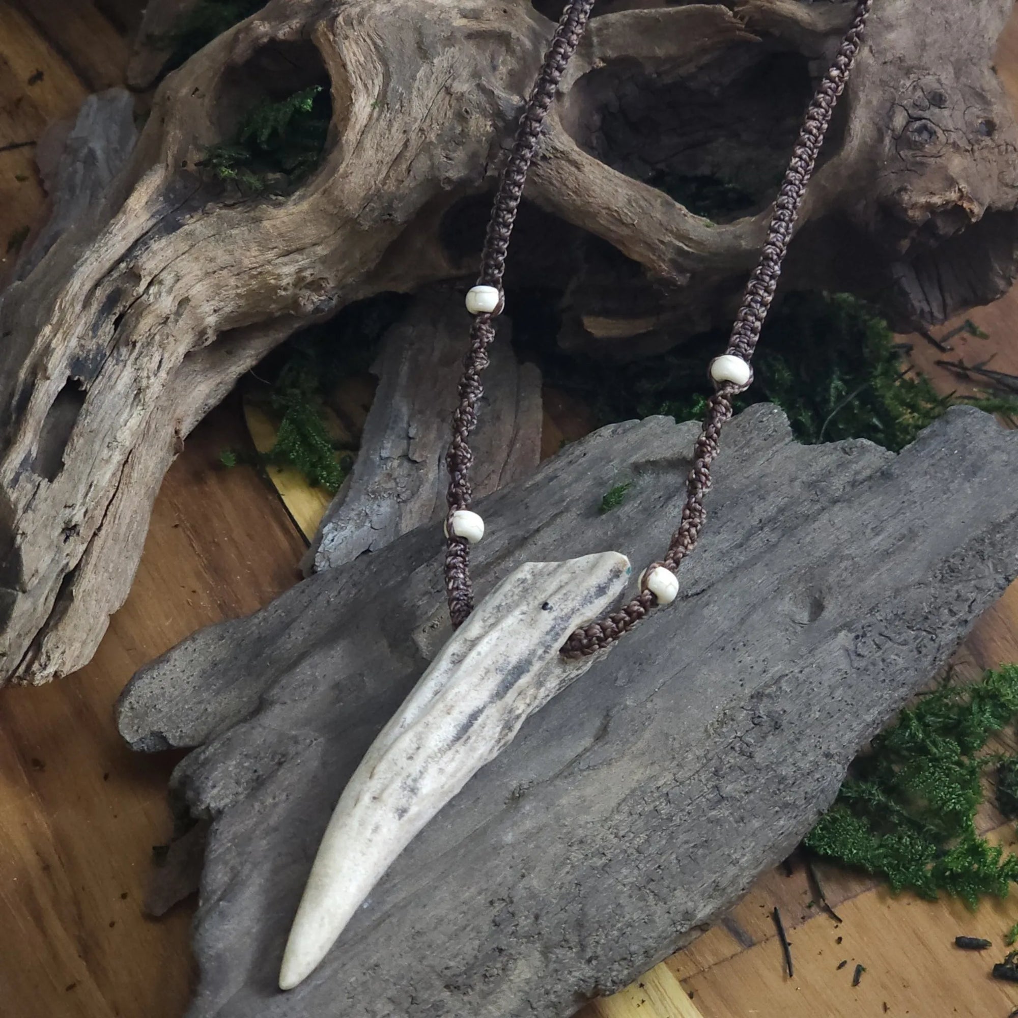 Necklace featuring deer antler tip and howlite beads, displayed on rustic wood background.