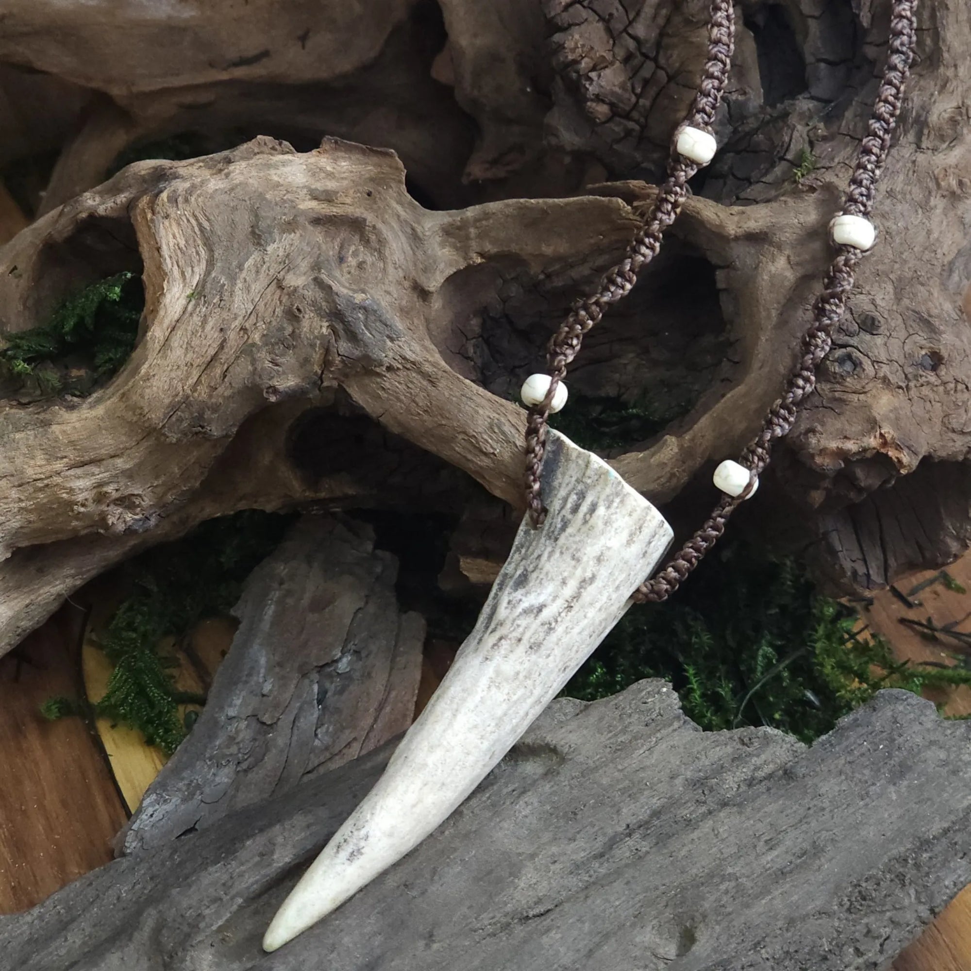 Pendant featuring deer antler tip and howlite beads, displayed on rustic wood background.
