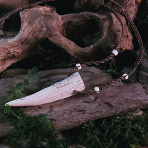 Necklace featuring deer antler tip and howlite beads, displayed on rustic wood background.