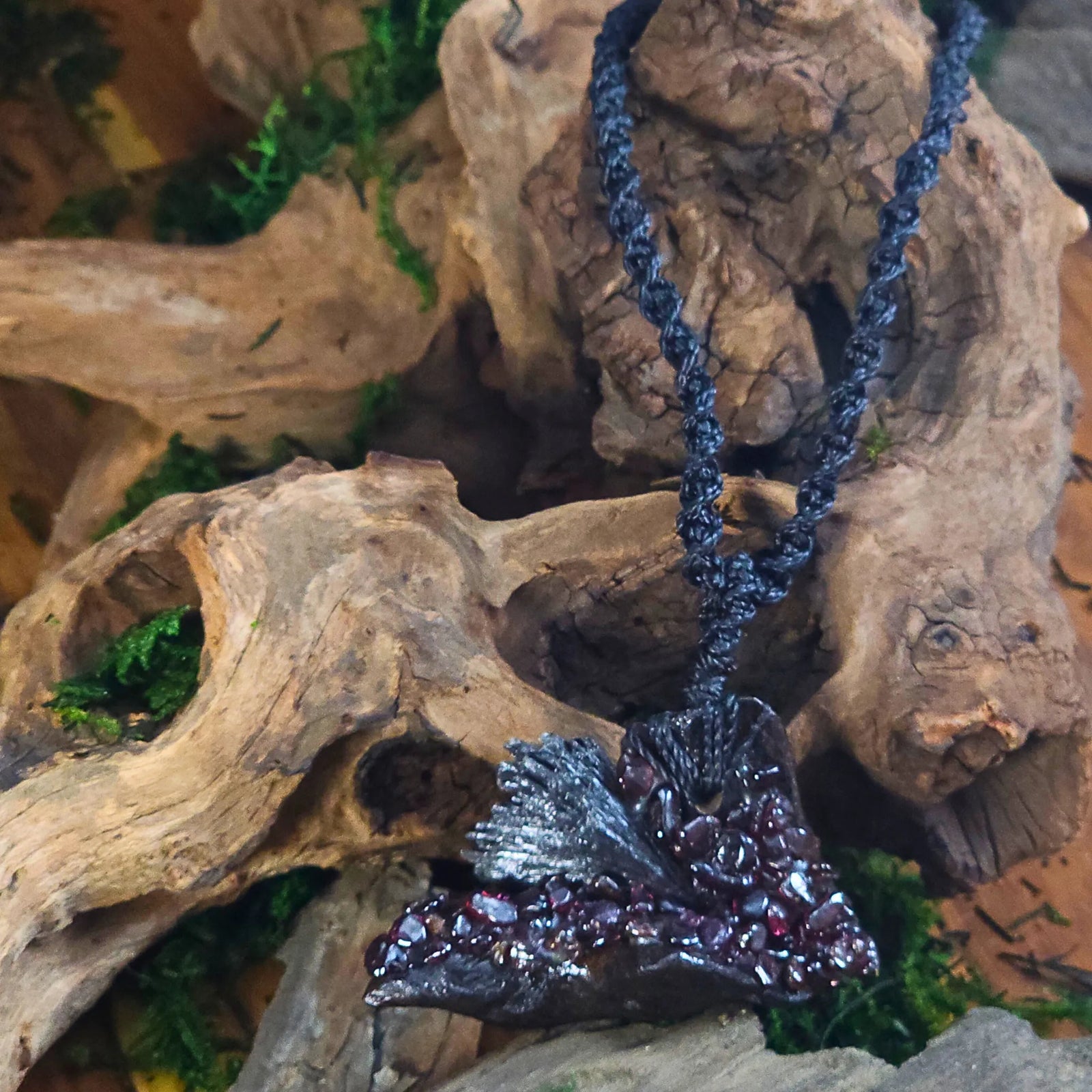 Front view of the Witch Queen’s Shield Talisman featuring a black kyanite blade with deep red garnet chips, set on driftwood and suspended from black woven cord.