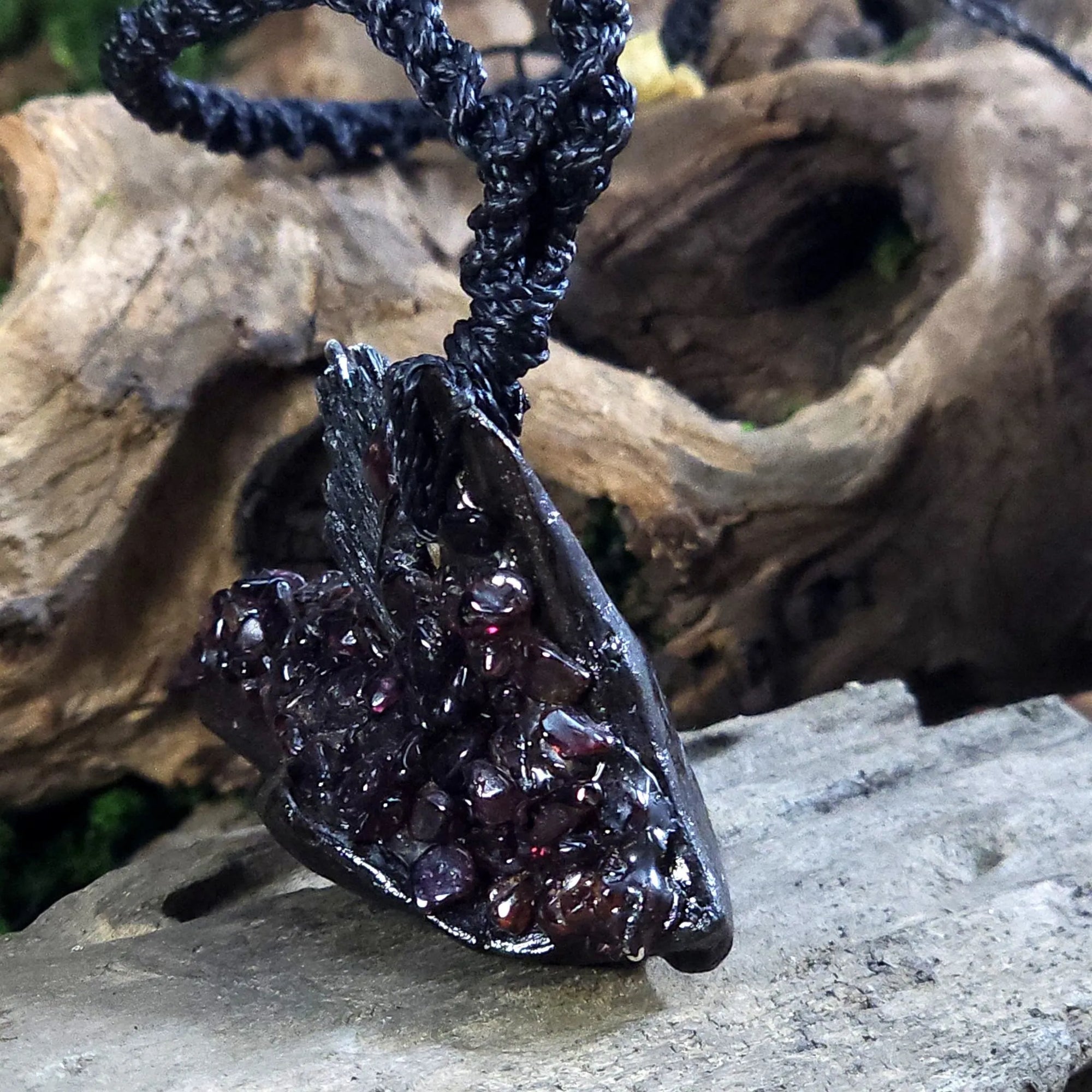 Side angle showing the layered texture of black kyanite and hand-placed garnet on rustic wood.